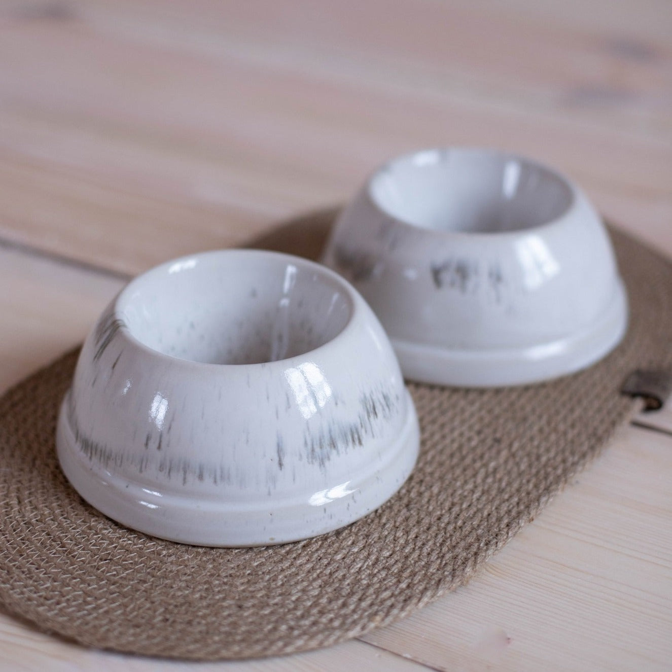 Elegant dog feeding set for spaniels. White speckled ceramic bowls with a jute mat keep feeding areas tidy and stylish.